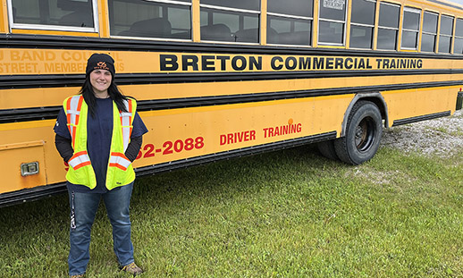 一个学生站在一辆公共汽车的前面与“布列塔尼的商业培训”写的。她穿牛仔裤、t恤、帽子和一个安全背心。